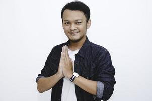 junger asiatischer mann, der trägt, geben grußhände. indonesischer Mann auf grauem Hintergrund. foto