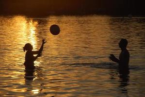 Paar beim Ballspielen im Meer bei Sonnenuntergang foto