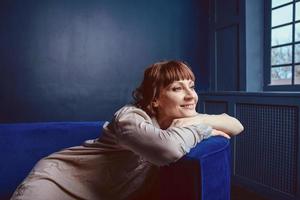 Schöne entspannte Frau zu Hause in der Nähe des blauen Sofas foto