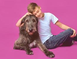 lächelnder fröhlicher elfjähriger Teenager in weißem T-Shirt und Jeans mit braunem großem Hund auf fuchsiafarbenem Hintergrund im Fotostudio. haustiere, freundschaftskonzept foto