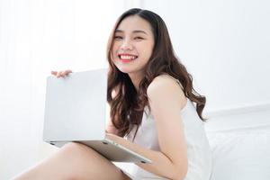 junge asiatische frau, die laptop im bett verwendet foto