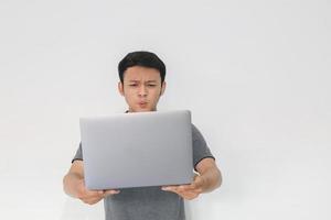 wow gesicht ihres asiatischen mannes schockiert, was er auf dem laptop auf isoliertem grauem hintergrund sieht. foto