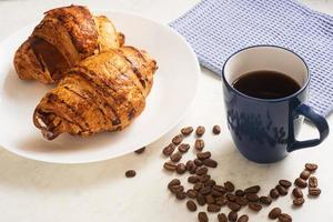 leckere, appetitliche, knusprige Croissants, heißer Kaffee in der blauen Tasse und Küchentuch auf Teller auf Marmortisch foto