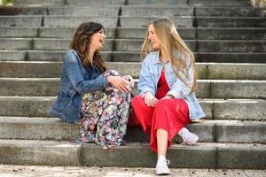 Zwei junge Frauen unterhalten sich und lachen auf städtischen Stufen foto