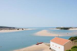 schöne luftaufnahme der alentejo-küste. Fluss, der zum Meer und Strand führt. nicht erkennbare menschen, die am strand wassersport betreiben. Portugal