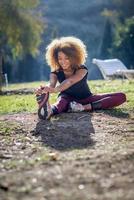 schwarze Fitness-Läuferin, die sich nach dem Lauf die Beine streckt foto