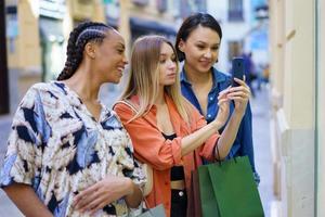modische gemischtrassige Damen, die beim Einkaufen in der Stadt ein Foto auf dem Smartphone machen