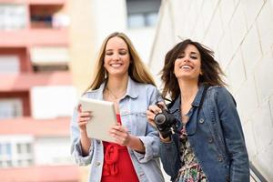 Zwei junge Touristenfrauen, die Karten mit digitalem Tablet im Freien suchen. foto