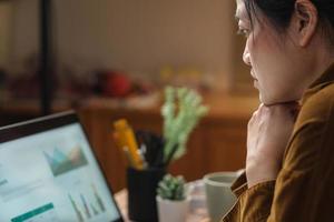 asiatische frau, die zu hause am laptop denkt und arbeitet foto