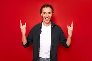 Aufgeregter Mann mit offenem Mund zeigt ein Rockzeichen mit seinen Händen, das das Hören seiner Lieblingsmusik Heavy Metal darstellt. isoliert auf rotem Hintergrund. Konzept - Menschen, Symbole, Rock and Roll, Freiheit foto