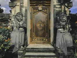 Tür oder Tor, um in die Details der traditionellen balinesischen Gartenarchitektur einzutreten. Indonesisches Holztor, bewacht von Steinstatuen. foto