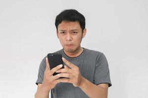 junger asiatischer mann weint und ist traurig, wenn er auf das smartphone schaut. Indonesien Mann trägt schwarzes Hemd isoliert grauen Hintergrund. foto