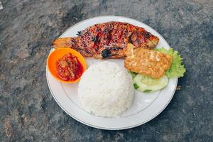 Köstlicher gegrillter Tilapia aus Indonesien mit Reis, Tempeh, Gemüse und Chilisauce im Teller foto