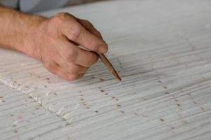 Hand mit einem Bleistift macht Spuren auf dem Teppich. Weben und Herstellung von handgefertigten Teppichen Nahaufnahme foto