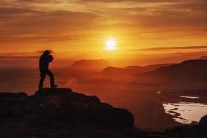 glücklicher Mann, der bei Sonnenuntergang auf einer Klippe steht foto