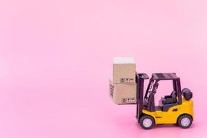 logistik und lieferservice - gabelstaplermodell und papierkartons oder paket mit einkaufswagenlogo auf rosa hintergrund. Einkaufsservice im Internet und bietet Lieferung nach Hause an.