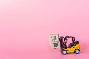 logistik und lieferservice - gabelstaplermodell und papierkartons oder paket mit einkaufswagenlogo auf rosa hintergrund. Einkaufsservice im Internet und bietet Lieferung nach Hause an. foto