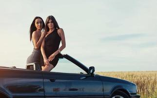 Mädchen, die in einem schwarzen Cabrio für die Kamera posieren foto