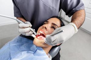 Hände eines Zahnarztes mit Handschuhen, die die Zähne eines Patienten in einer Klinik reinigen foto