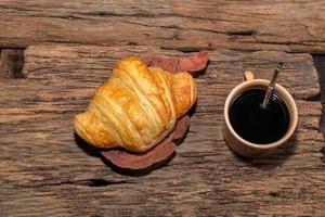 frühstückscroissant in teller und kaffee auf holztisch. foto