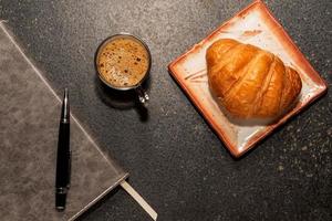 frühstückscroissant in teller und kaffee auf steintisch. foto