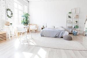 stilvolles Loft-Schlafzimmer-Interieur. Geräumiges Design-Apartment mit hellen Wänden, großen Fenstern, großem Bett. saubere moderne dekoration mit eleganten möbeln im minimalistischen skandinavischen stil. foto