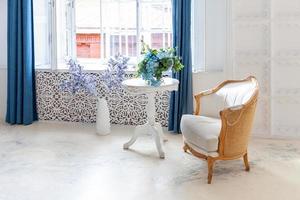 Wunderschönes, klassisches, weißes, helles, sauberes Luxus-Schlafzimmer im Barockstil mit großem Fenster, Sessel und Blumenkomposition. foto