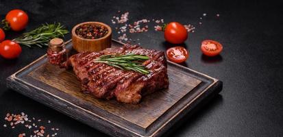 Gegrilltes Ribeye-Rindsteak, Kräuter und Gewürze auf einem dunklen Tisch foto