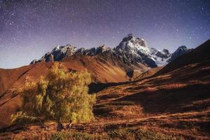 fantastischer Sternenhimmel. Herbstlandschaft und schneebedeckte Gipfel foto