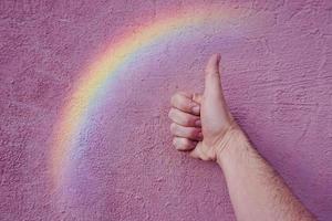 Hand mit einem Regenbogen an der rosa Wand. lgbt-symbol foto