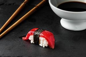 Roter Thunfisch-Nigiri mit Nori-Algen auf schwarzem Schieferstein mit Essstäbchen und Schüssel mit Sojasauce. roher Fisch im traditionellen japanischen Sushi-Stil. horizontales Bild. foto