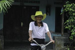 ein porträt eines indonesischen alten bauern trägt einen gelben hut mit einem alten fahrrad foto