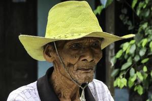 ein porträt eines indonesischen alten bauern trägt einen gelben hut mit einem alten fahrrad foto