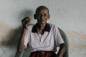 Nahaufnahme des Porträts eines asiatischen javanischen alten Mannes mit einer Zigarette in der Hand foto