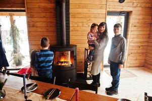 mutter und vier kinder in einem modernen holzhaus an tisch und kamin verbringen zeit zusammen in warmer und liebe. foto