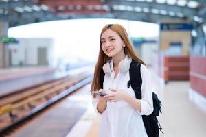 junges asiatisches mädchen, das am bahnhof auf den zug wartet foto