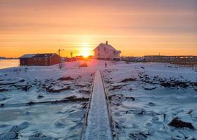 Sonnenaufgang über nordischem Haus und Holzbrücke an der Küste im Winter auf den Lofoten-Inseln foto