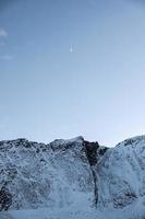 schneebedeckter Berg und Halbmond im blauen Himmel in Skandinavien foto