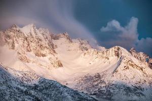 goldener sonnenaufgang auf schneeberg mit wolken, die auf grat wehen foto