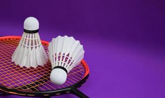 Weißer cremefarbener Badminton-Federball vor Badmintonschlägern auf violettem Boden des Indoor-Badmintonplatzes, weicher und selektiver Fokus auf Federball, Konzept für Badminton-Sportliebhaber auf der ganzen Welt foto