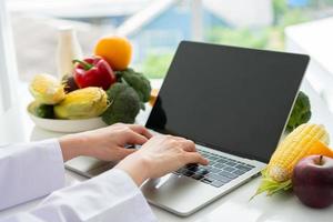 porträt einer asiatischen lächelnden ernährungsberaterin, die auf einem laptop-computer einen ausgewogenen korrekturdiätplan für patienten- oder gewichtsverlustratschläge tippt. konzept des gesunden lebensstils, der gesunden ernährung, der diät foto