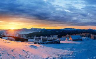 fantastischer Sonnenuntergang über schneebedeckten Bergen und Holzchalets foto