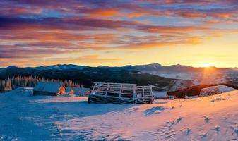 fantastischer Sonnenuntergang über schneebedeckten Bergen und Holzchalets. foto