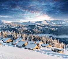 fantastischer Sonnenuntergang über schneebedeckten Bergen und Holzchalets foto