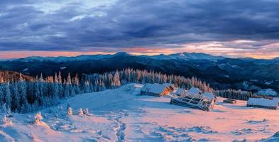 fantastischer Sonnenuntergang über schneebedeckten Bergen und Holzchalets. foto