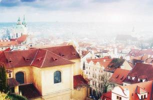 das rote dach in prag. Panoramablick von der Burg, Tschechische Republik. sommertag mit blauen himmelwolken und dichtem nebel in der stadt. foto