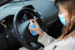 Sprühen von antibakteriellem Desinfektionsspray im Auto, Infektionskontrollkonzept. Desinfektionsmittel zur Vorbeugung von Coronavirus, Covid-19, Grippe. Sprühflasche. Frau, die eine medizinische Schutzmaske trägt, die ein Auto fährt.