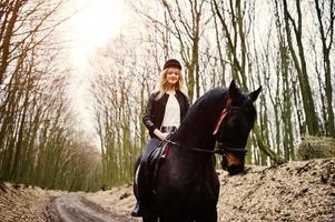 junges stilvolles blondes mädchen, das auf pferden im herbstwald reitet. foto