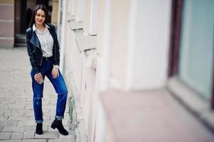 Porträt stilvoller Kleidung junger Mädchen auf Lederjacke und zerrissenen Jeans mit Handy zur Hand. Straßenmode-Model-Stil. foto