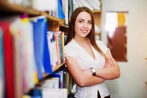 brünettes mädchen in der bibliothek, trägt weiße bluse und schwarzen minirock. sexy Geschäftsfrau oder Lehrerkonzept. Lächeln auf Zahnspangen. foto